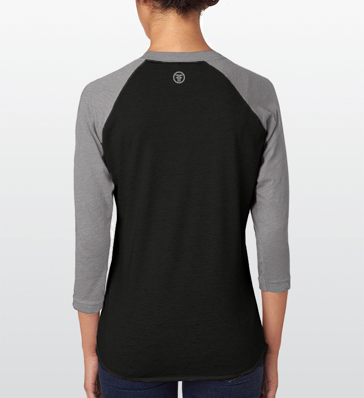 Back of a lady wearing a heather black baseball t-shirt that has heather grey arms and collar.  A grey logo is below the collar that has two Fs, back to back, with a circle around it.