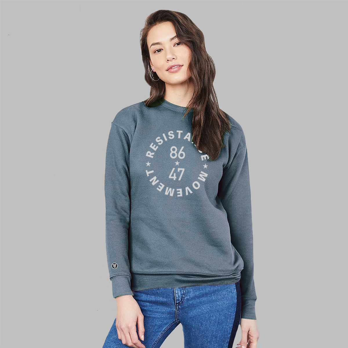 A lady wearing a a Heather Slate Blue, unisex political crew sweatshirt. The grey text says "86 47"in the middle with"Resistance Movement" around it.