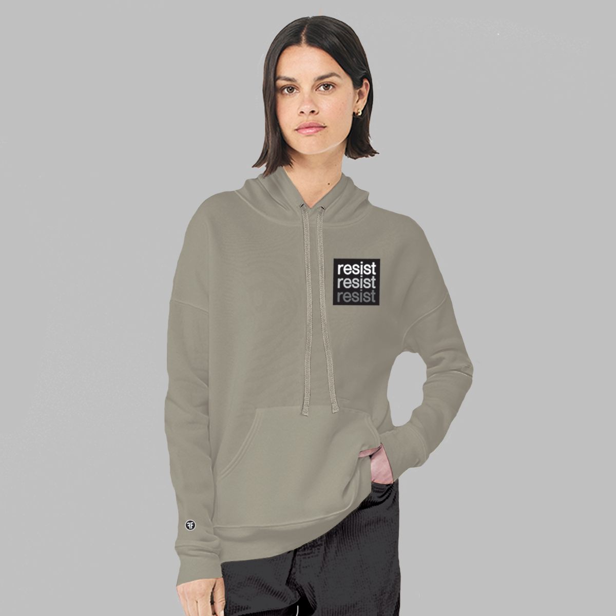 A lady wearing a stone taupe, unisex political hoodie. The logo is a left chest black square, with text that says Resist, three times in white, light grey and dark grey.  