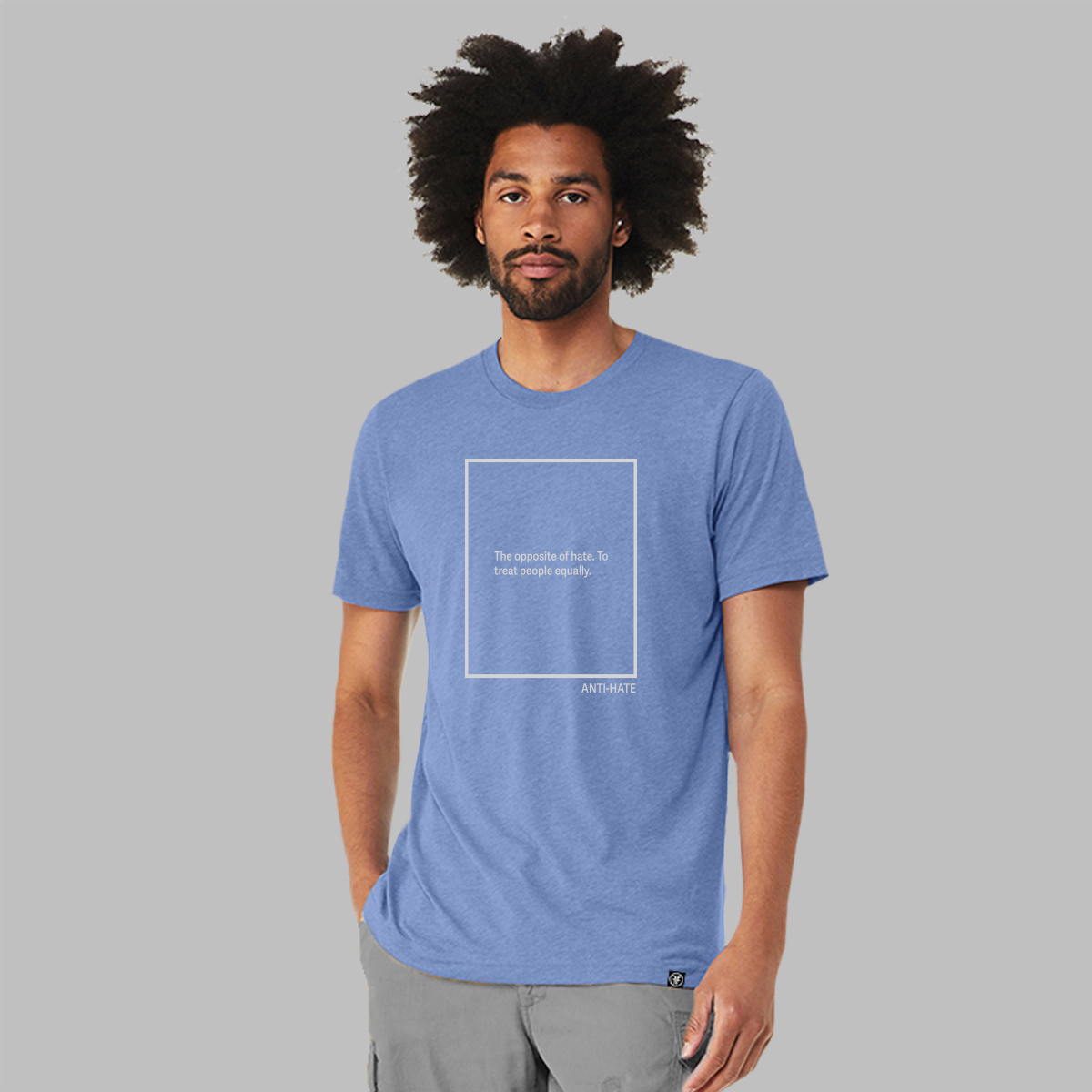 A man wearing a heather blue unisex tshirt with the outline of a grey rectangle. Inside the text says, the opposite of hate, to treat people equality. The word anti-hate is in the lower left corner.