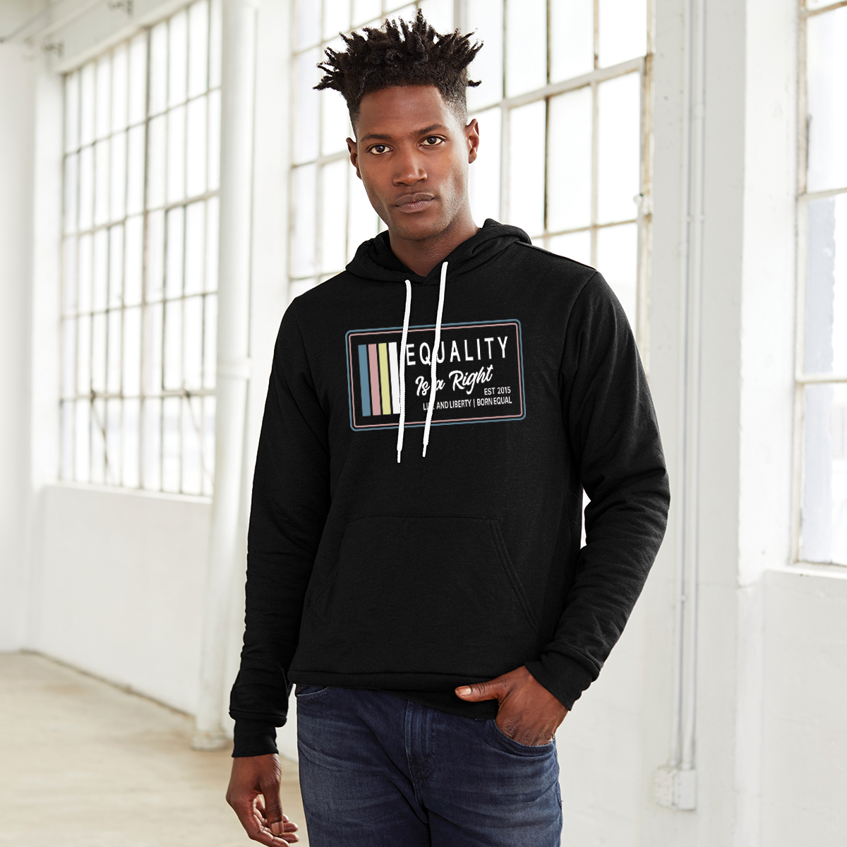 Man wearing a black hoodie with the text, Equality, Life and Liberty, and Born Equal, in white bold font. The text, Is a Right, is in white script font. On the side of the logo are stripes of the colors Slate Blue, Dusty Rose, Bisque Gold, and white.