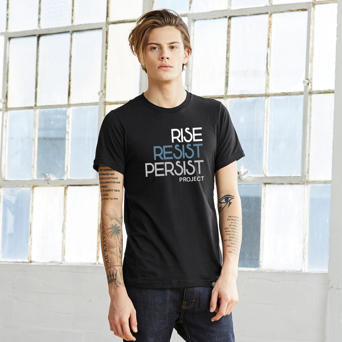 A man wearing a political unisex black t-shirt. The text says Rise, Resist, Persist, Project. The font is white, Slate Blue, and grey.