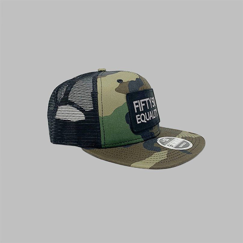 The side view of a camouflage, flat bill, snapback equality hat. It shows black mesh side panels, and a sewn on black patch that has the embroidered text Fifty50, Equality, in bold, grey font.
